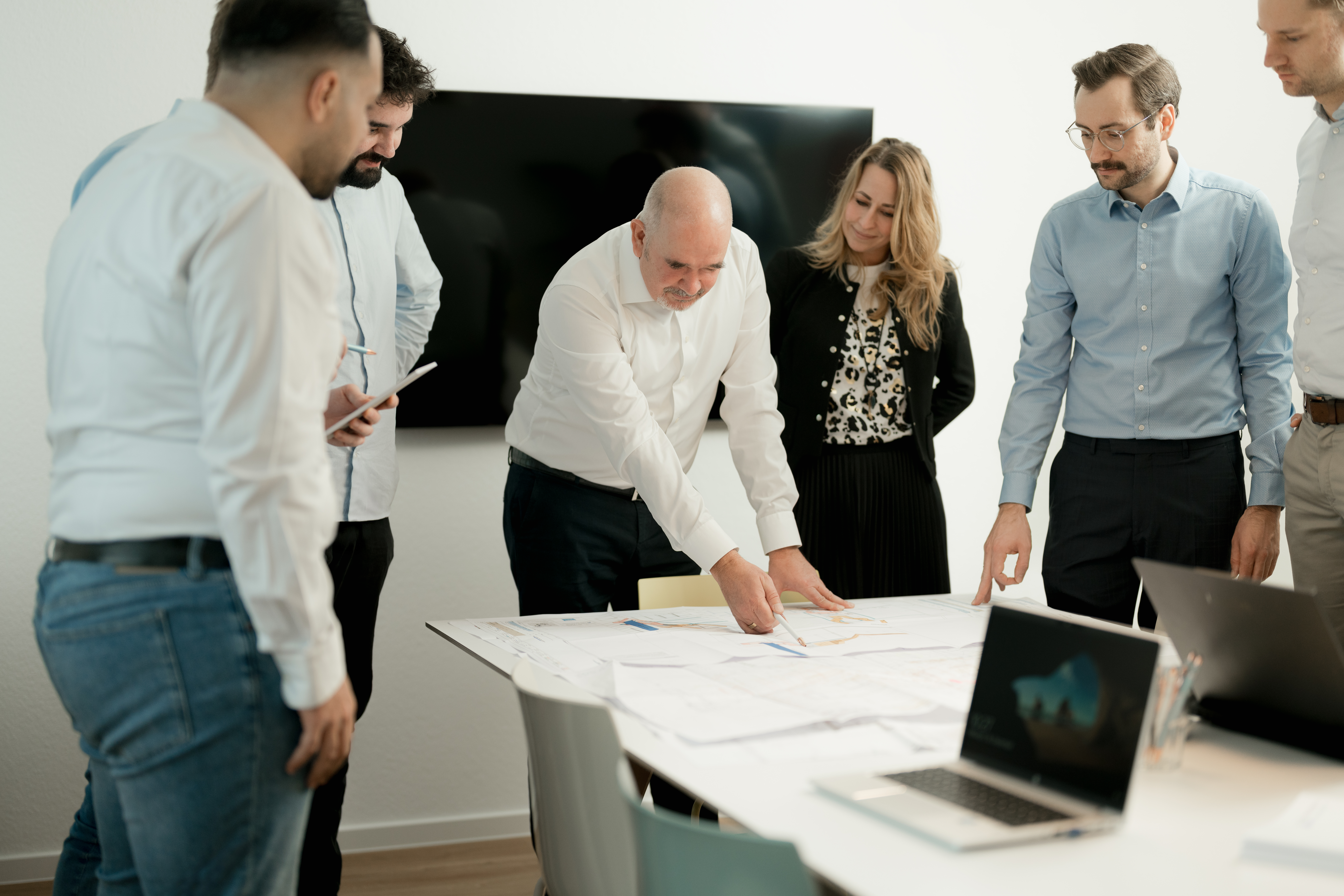 Content Fotograf, ein Herr in einer Firma, der seinen Angestellten in der Firma, Pläne erklärt, die auf dem Tisch liegen.