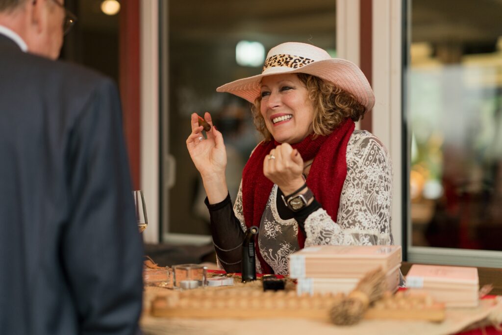 Content Fotograf, eine Dame am Tisch sitzend. Sie trägt einen Hut und raucht eine Zigarette.