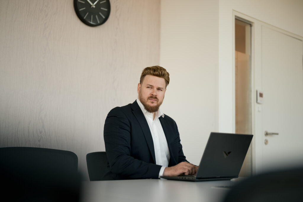 Content Fotograf, Business Mann im Anzug. Er sitzt an einem Tisch und schreibt an seinem Laptop.