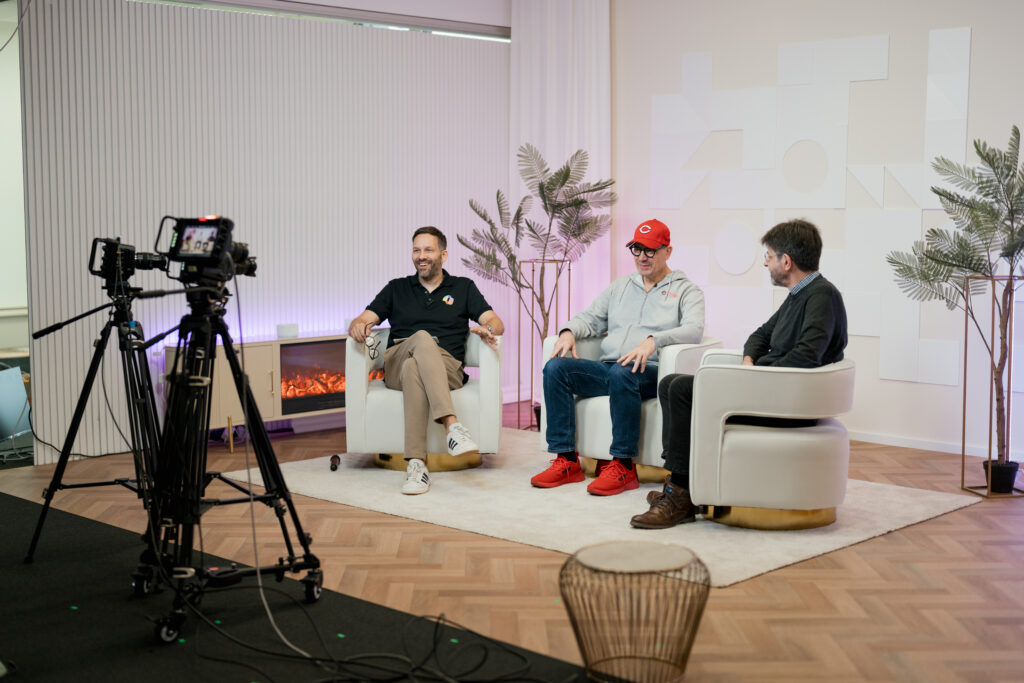 Content Fotograf, drei Herren, die auf Sesseln sitzen und miteinander reden. Vor ihnen ist eine Kamera aufgebaut