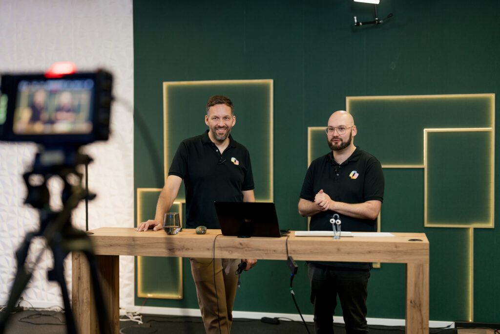 Content Fotograf, zwei Herren, die vor einem Tisch stehen und etwas in eine Kamera sprechen.