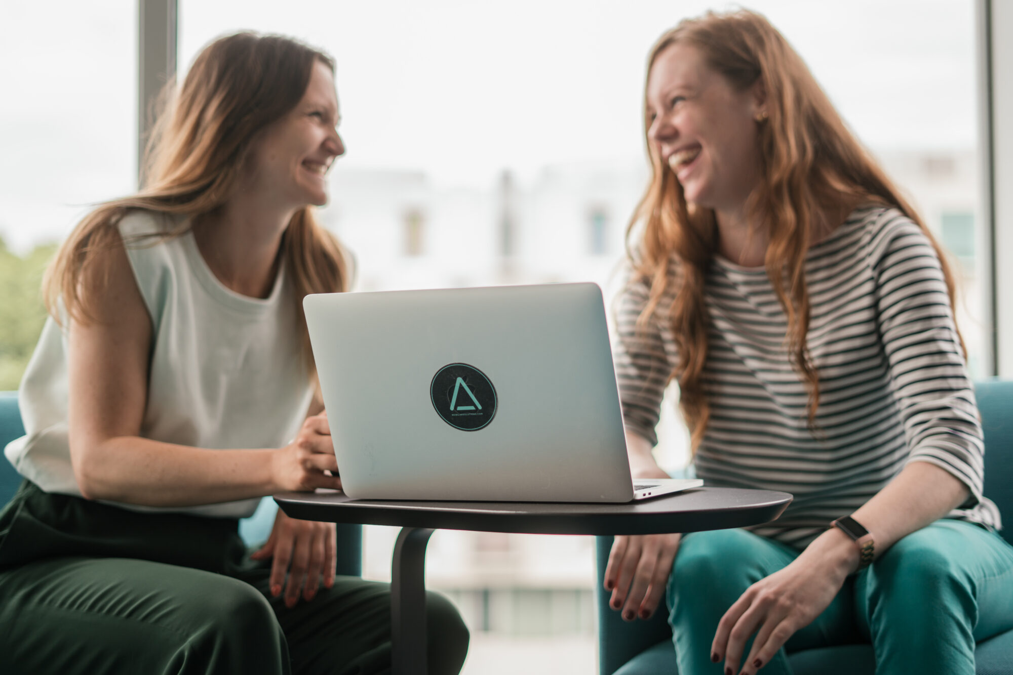 Zwei Frauen sitzen gemeinsam an einem Laptop und sprechen miteinander.