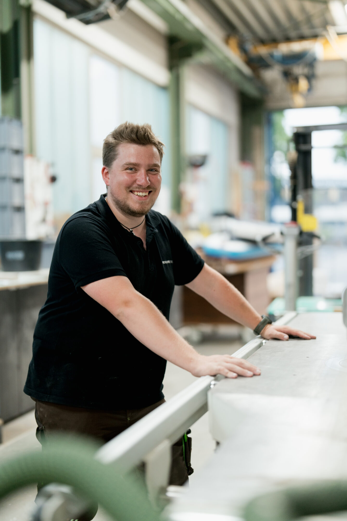 Mann arbeitet in einer Tischlerwerkstatt und blickt lächelnd in Kamera. - Mitarbeiterfotos für Unternehmen