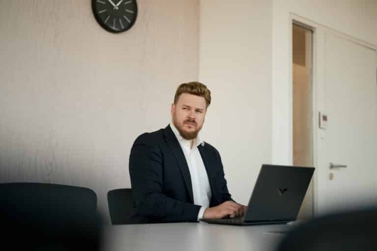 Willkommen bei Content-Fotograf 7 Content Fotograf, Business Mann im Anzug. Er sitzt an einem Tisch und schreibt an seinem Laptop.