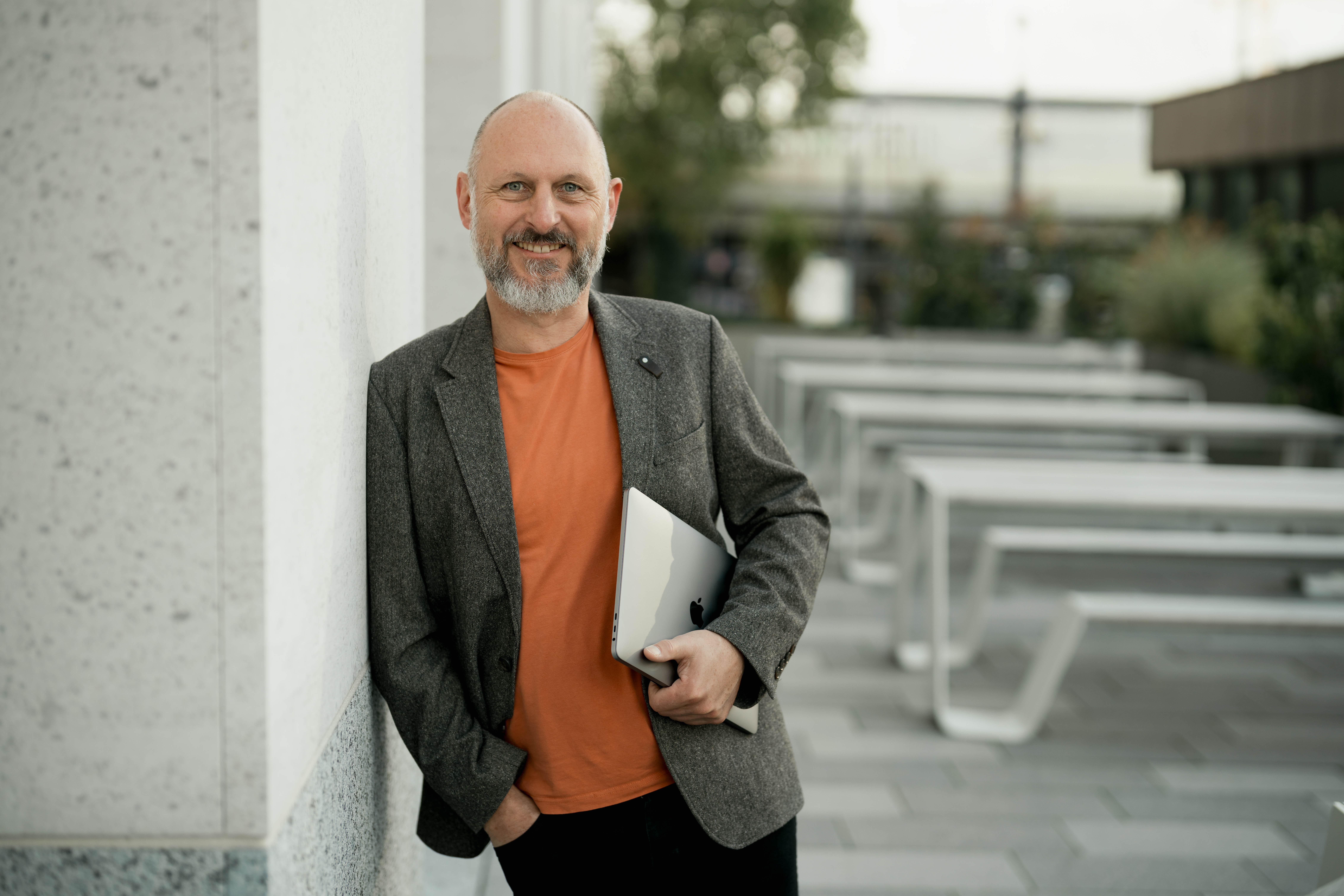 Portaitbild eines Business-Mannes, der sich locker an eine Wand lehnt und einen Hefter in der Hand hält - employer branding