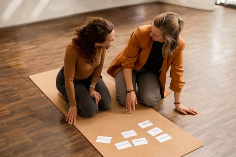 Content Planung für Social Media 3 Zwei Frauen sitzen kniend auf einer Yogamatte und planen etwas mit Karteikarten.