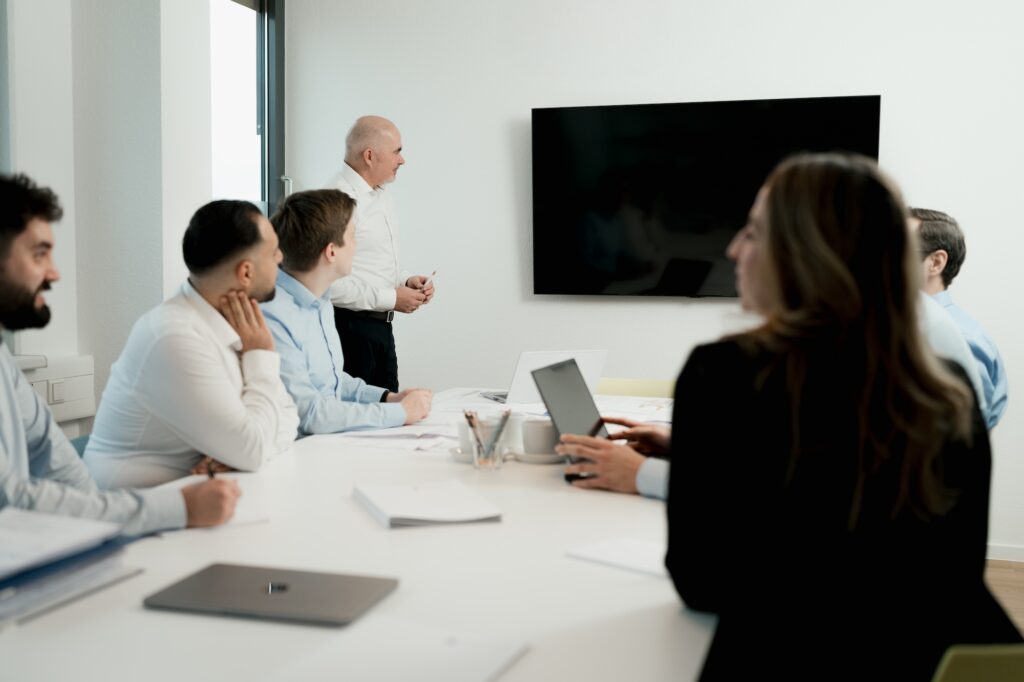 Authentische Fotos im Marketing: Warum echter Content Stockfotos schlägt 2 Unternehmensteam in einem Meeting in einem Büro, bei dem der Leiter eine Präsentation an einem großen Bildschirm hält. - Authentische Fotos im Marketing